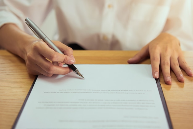 Woman signing document and hand holding pen putting signature at paper, order to authorize their rights.