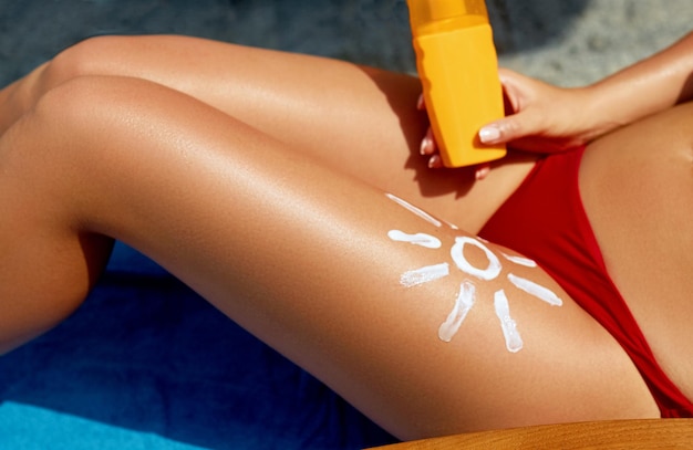 Woman sunbathing on the beach Closeup view on the legs with lotion sun shape