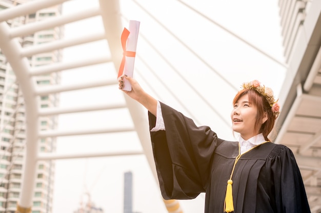 Photo woman wearing academic gown raising hand with success bachelor degree of university