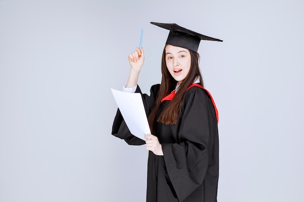 Woman wearing graduation cap holding pen and empty sheet. High quality photo