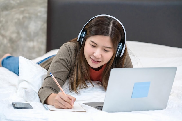 Photo woman writing while working at laptop on bed