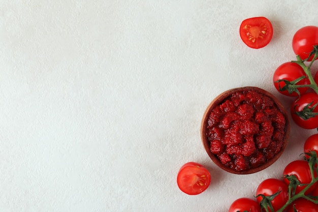 Wooden bowl with tomato paste and tomatoes on white textured table