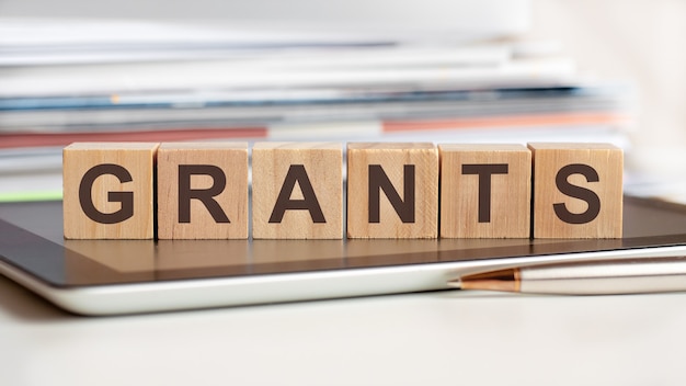 The word grants is written on wooden cubes standing on a notepad, in the surface a stack of documents