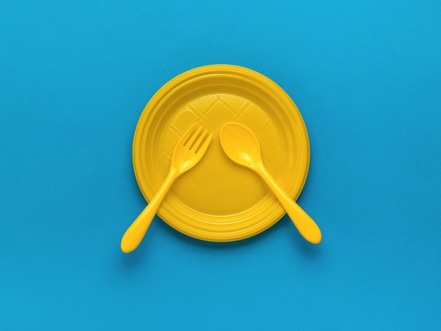 Yellow forks and a spoon in a yellow plastic bowl on a blue background Flat lay