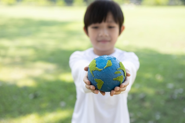 Photo young asian boy holding planet earth globe at natural park background gyre