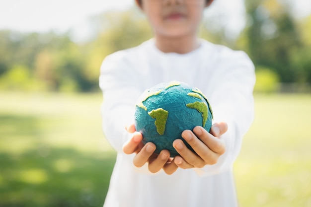 Photo young asian boy holding planet earth globe at natural park background gyre