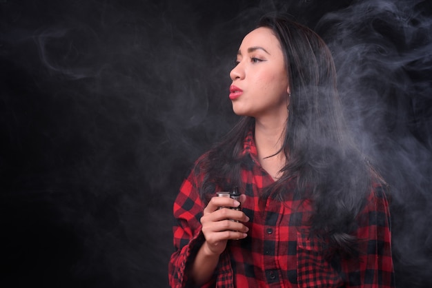 Photo  young beautiful filipino woman vaping against black wall