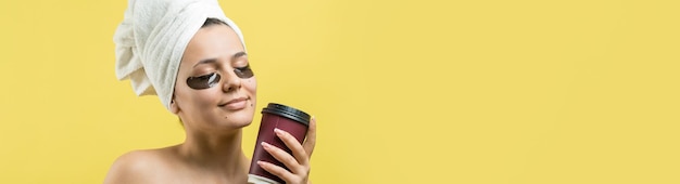 Young beautiful girl in a white towel on his head wears collagen gel patches under her eyes Mask under eyes treatment face The girl holds a glass of coffee in her hands