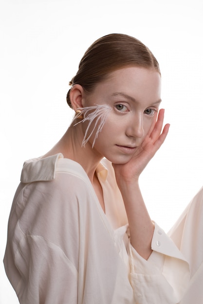 Photo young blonde model with art makeup in white outfit posing in white studio