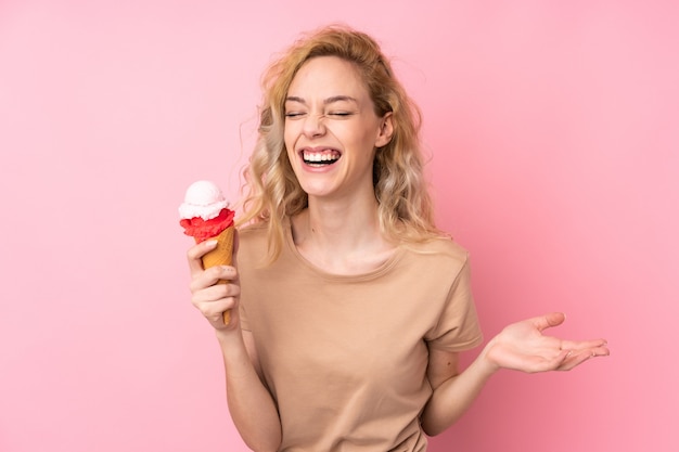 Young blonde woman holding a cornet ice cream isolated on pink wall