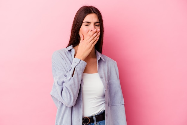 Young caucasian woman isolated on pink wall yawning showing a tired gesture covering mouth with hand.