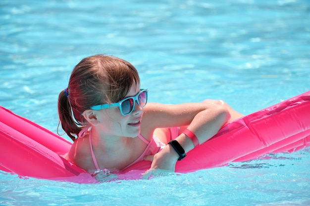 Young child girl relaxing on summer sun swimming on inflatable air mattress in swimming pool during tropical vacations Summertime activities concept