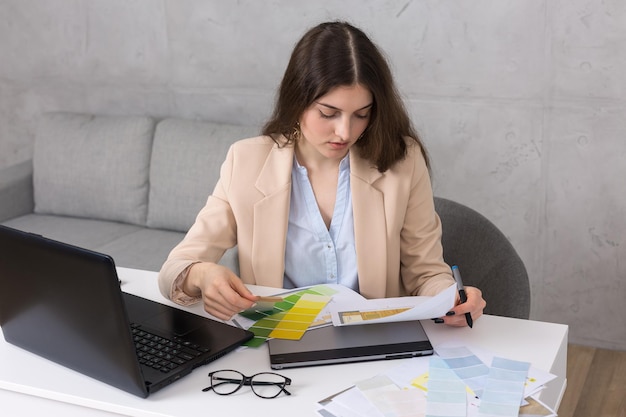 A young designer girl sitting at a table draws on a tablet Makes business calculations on the computer