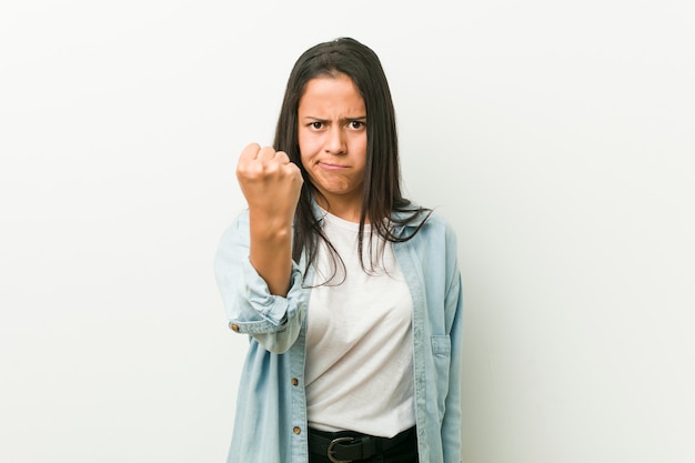 Young hispanic woman showing fist in, aggressive facial expression.