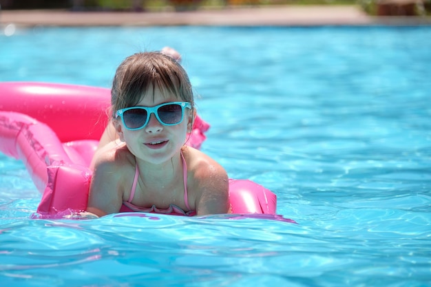 Young joyful child girl having fun swimming on inflatable air mattress in swimming pool with blue water on warm summer day on tropical vacations Summertime activities concept