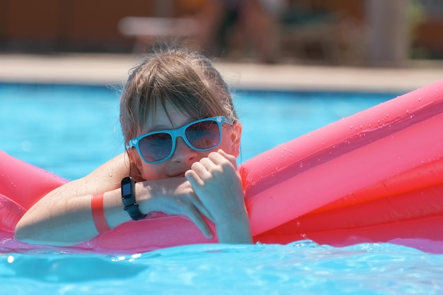 Young joyful child girl having fun swimming on inflatable air mattress in swimming pool with blue water on warm summer day on tropical vacations Summertime activities concept