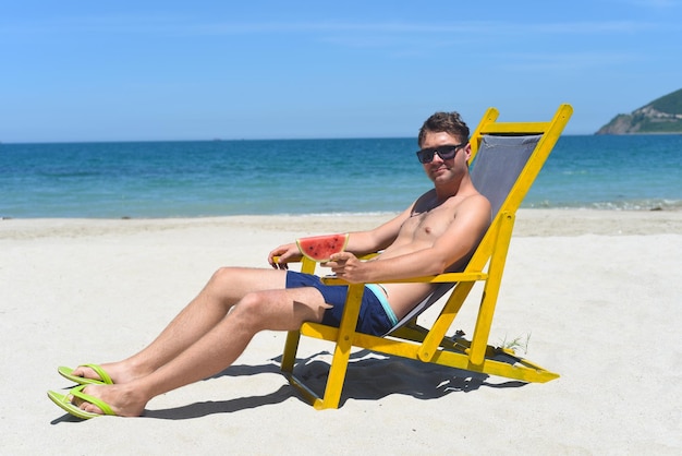 Young man eating watermelon on a white sandy beach in Vietnam