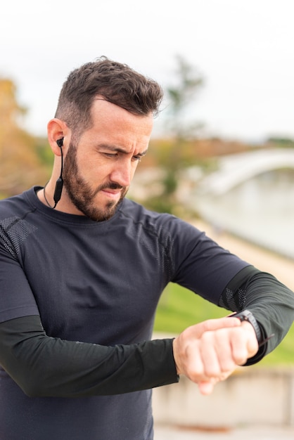 Young runner man with headphones training and checking stopwatch.