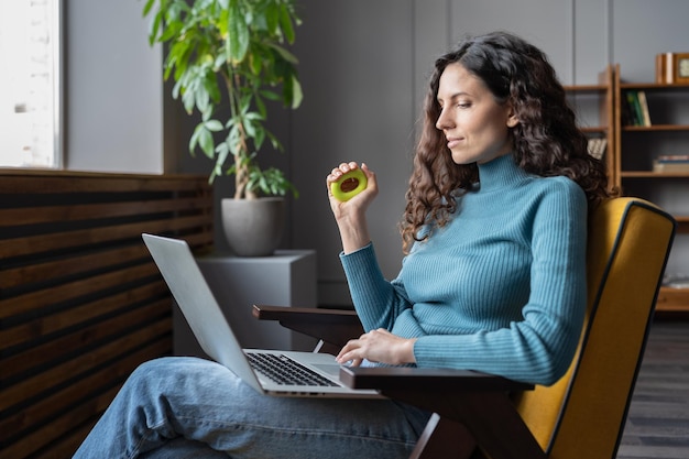 Young satisfied female employee squeezing carpal expander in hand and looking at laptop screen