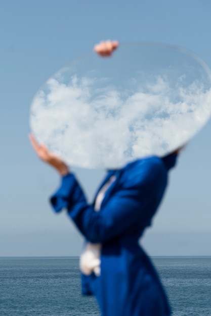 Young woman in blue suit posing with mirror against blue sky