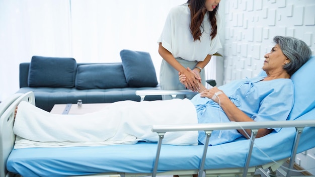 Young woman holding hands to support Sick mother receiving saline in bed in the hospital room