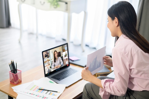 Photo young woman is working with her computer screen while business meeting through video conferencing application .