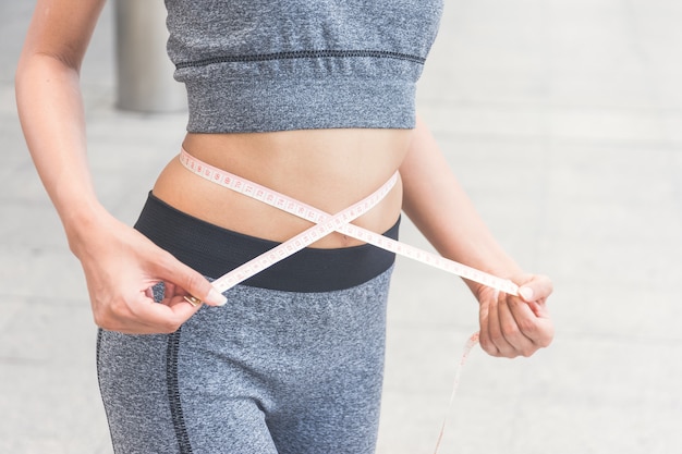 Photo young woman measuring her waist with a tape measure