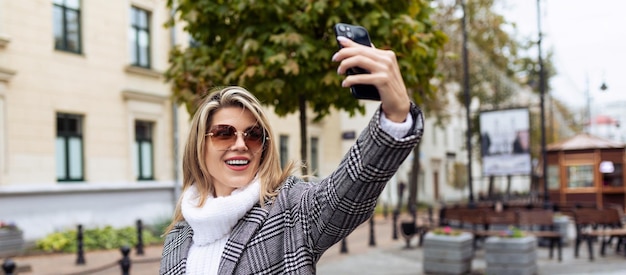 Young woman model taking selfie with phone outdoors in spring