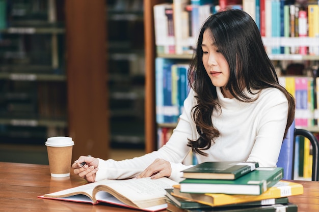 Photo young woman reading book while sitting in library