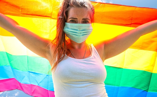 Young woman waving a rainbow flag for LGBT rights, freedom for homosexual Lgbtq concept, wearing a safety mask for Covid-19, coronavirus. Protesting and coronavirus