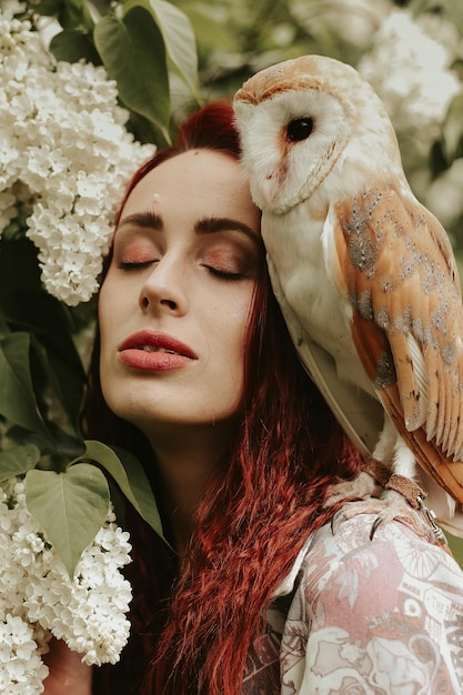 Young woman with red hair in a lilac garden with an owl barn owl