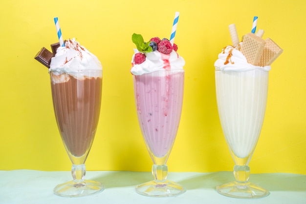 Foto zomerse verfrissende drankjes, milkshakes, gekke shakes met ijs, bessen, vanille, chocolade. op een helderblauwe gele achtergrond