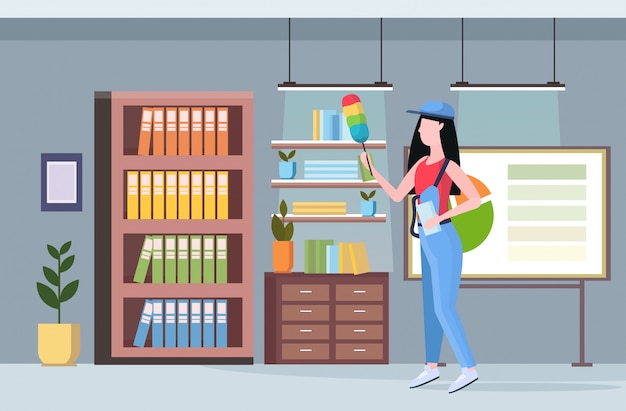 woman cleaner in uniform holding dust brush female janitor dusting bookshelves professional cleaning service concept creative co-working center modern office interior full length flat horizontal