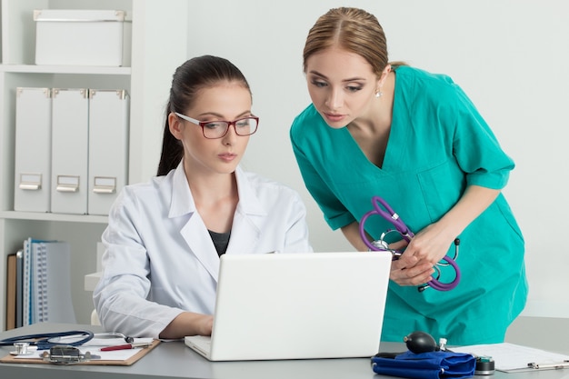 Dwóch pięknych kobiet lekarzy medycyny patrząc na monitorze laptopa stojącego w ich biurze. Pojęcie medyczne i opieki zdrowotnej