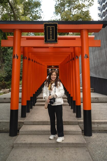 Zdjęcie kobieta stoi przed pomarańczową bramą torii.