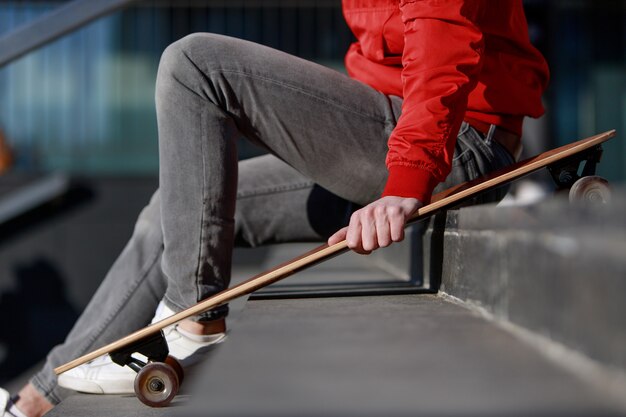 Longboarder mężczyzna w przypadkowych ubraniach spoczywa na schodach, siedząc z longboard / deskorolka na zewnątrz