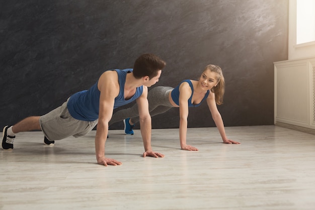 Młody mężczyzna i kobieta trening w klubie fitness. Para fitness wykonująca ćwiczenia z deski lub pompek, trening w pomieszczeniu, kopia przestrzeń