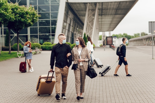 Zdjęcie młody mężczyzna i kobieta w maskach ochronnych z walizką jadą na lotnisko