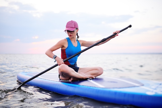 Piękna młoda dziewczyna w sportowej siedzi na pokładzie SUP