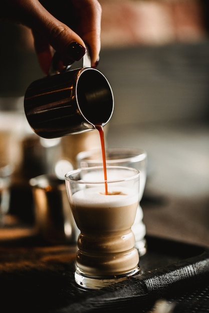 Zdjęcie ręka robi pić kawie w kawiarni barista. filiżanka tradycyjnego espresso z mlekiem. kawa nalewa do kieliszków. stonowany obraz