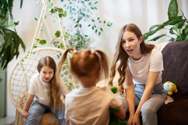 Zdjęcie wściekła młoda matka skarci małą córkę i nastoletnią siostrę oglądającą w tle w pokoju w