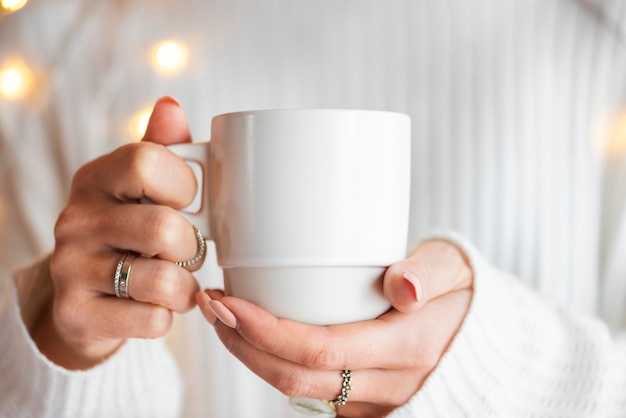 Femme dans un pull blanc avec une maquette de tasse blanche