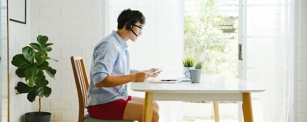 Gratis Foto aziatische zakenman gekleed in shirt en korte broek laptop praten met collega's in videogesprek tijdens het werken vanuit huis in de woonkamer. zelfisolatie, sociale afstand nemen, quarantaine voor coronaviruspreventie.