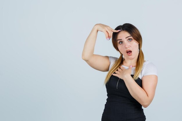 Jonge vrouw die één hand op de borst houdt terwijl ze de wijsvinger op het hoofd legt