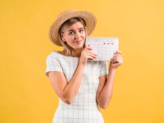 Gratis Foto mooie jonge vrouw die met hoed een periodekalender houdt