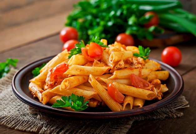 Gratis foto penne pasta in tomatensaus met kip en tomaten op een houten tafel