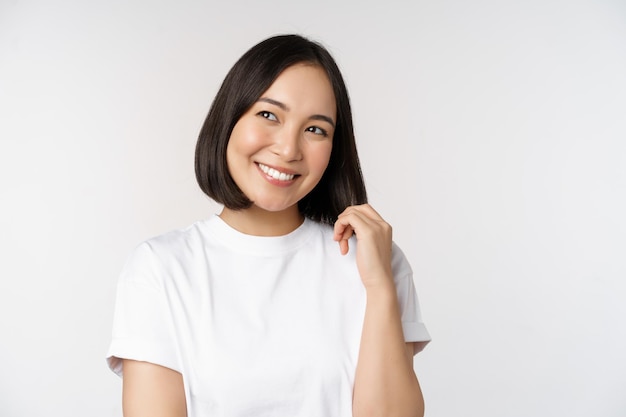 Gratis Foto portret van een schattige, kokette vrouw die lacht en glimlacht terwijl ze opzij kijkt doordacht denken of zich inbeeldt in een wit t-shirt over de achtergrond van de studio