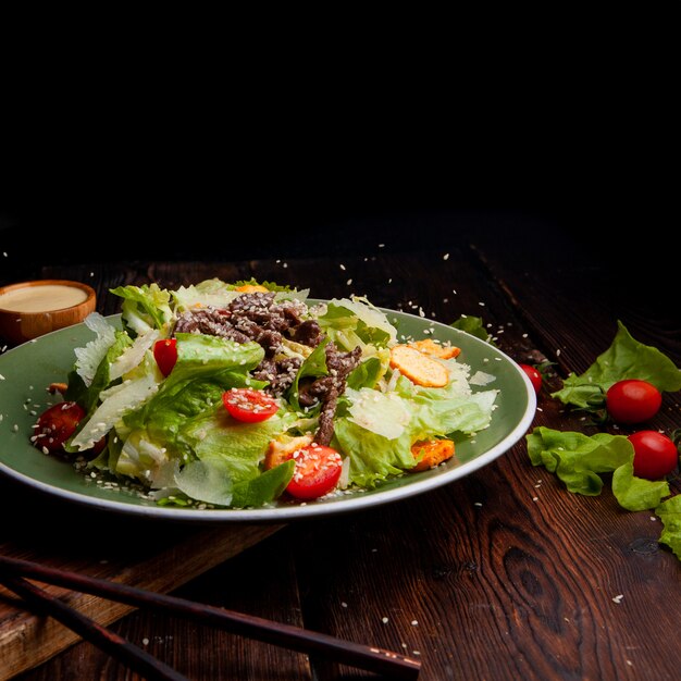 Rijst het gieten op heerlijke salademaaltijd in een plaat met eetstokjes op een houten en zwart zijaanzicht als achtergrond. ruimte voor tekst