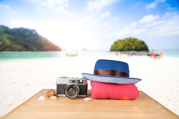 Gratis foto rode roze toren, blauwe hoed, oude vintage camera en schelpen over houten vloer op zonneschijn blauwe hemel en oceaan achtergrond