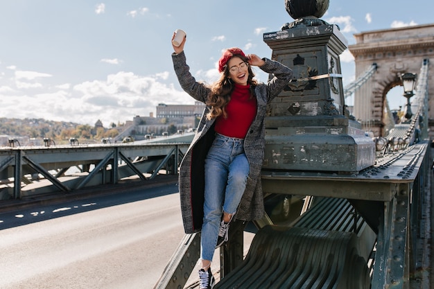 Gratis Foto slanke lachende vrouw in vintage jeans poseren op het platform achtergrond in zonnige dag in parijs